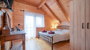 Ein gemütliches Schlafzimmer in einer Blockhütte mit einem Holzbett, einem Schreibtisch und einem Fenster mit Vorhängen.