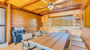 Ein Holzhütten-Interieur mit Esstisch, Stühlen, Grill und Deckenventilator.