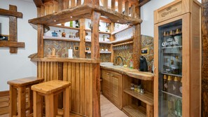A rustic wooden bar area with stools, shelves with glassware, and a refrigerator stocked with beverages. - Villa Luna - Ludbreg by Villas Guide (Ludbreg)