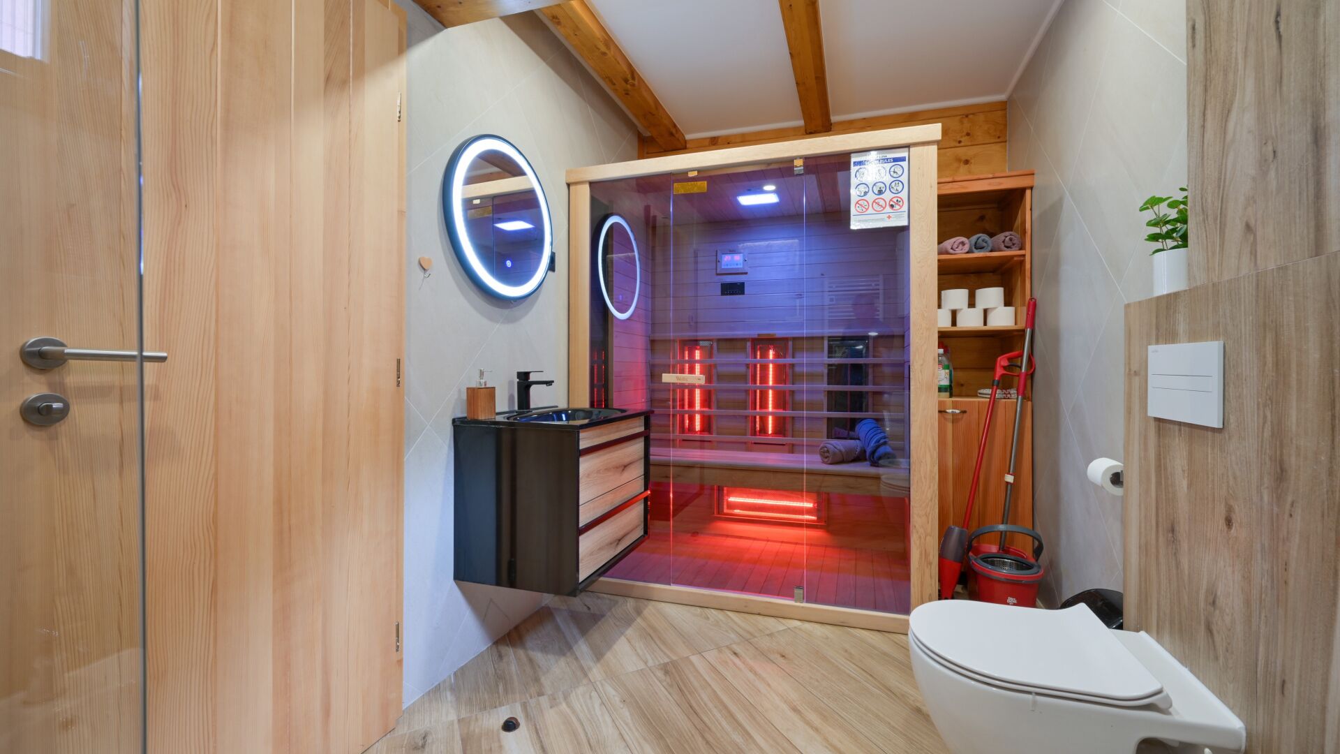 Une petite salle de bain avec un meuble-lavabo en bois, des toilettes et un espace douche éclairé de lumières rouges.