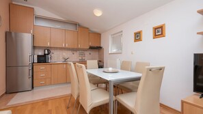 A compact kitchen with wooden cabinets, a stainless steel refrigerator, a dining table with four chairs, and a black television on a wooden stand. - Apartman Fortuna pool-Makarska by Villas Guide (Makarska)