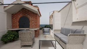 Een balkon met een bakstenen open haard, rieten meubels en uitzicht op de stad.