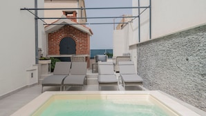 Een dakterras met een zwembad, lounge fauteuils en een metselwerk openhaard.
