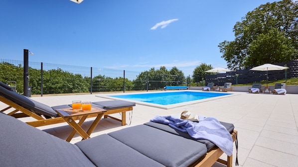 A poolside area with lounge chairs, a table with drinks, and a fenced pool.