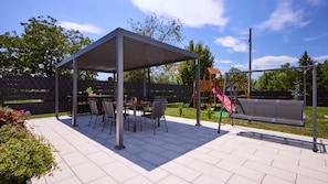 A covered patio with a table and chairs, a swing set, and a fenced play area.