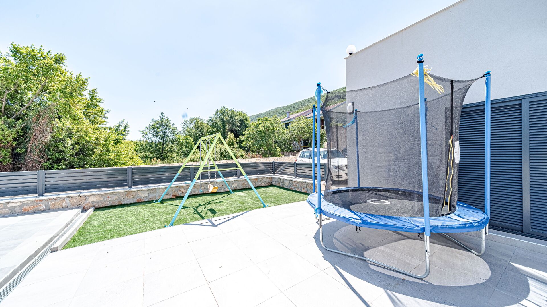 A rooftop with a trampoline, a swing set, and a view of a hilly landscape.