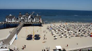 Ein Strandhotel mit Steg, Strandsonnenschirmen und Liegestühlen.
