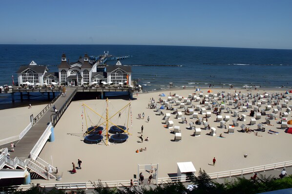 A beachside hotel with a pier, beach umbrellas, and sun loungers.