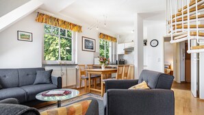 A modern living room with a sofa, armchair, and coffee table, a dining area with a table and chairs, and a kitchen in the background. - Apartment '22' with Balcony and Wi-Fi (Sellin)