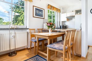 A modern kitchen with a dining table, chairs, a radiator, and a window with a view of greenery.
