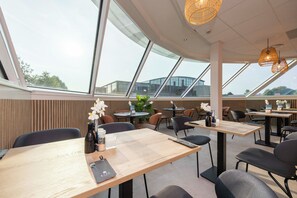 Guests can dine in style with tables and chairs arranged for comfort, surrounded by large windows offering views of the surrounding landscape.