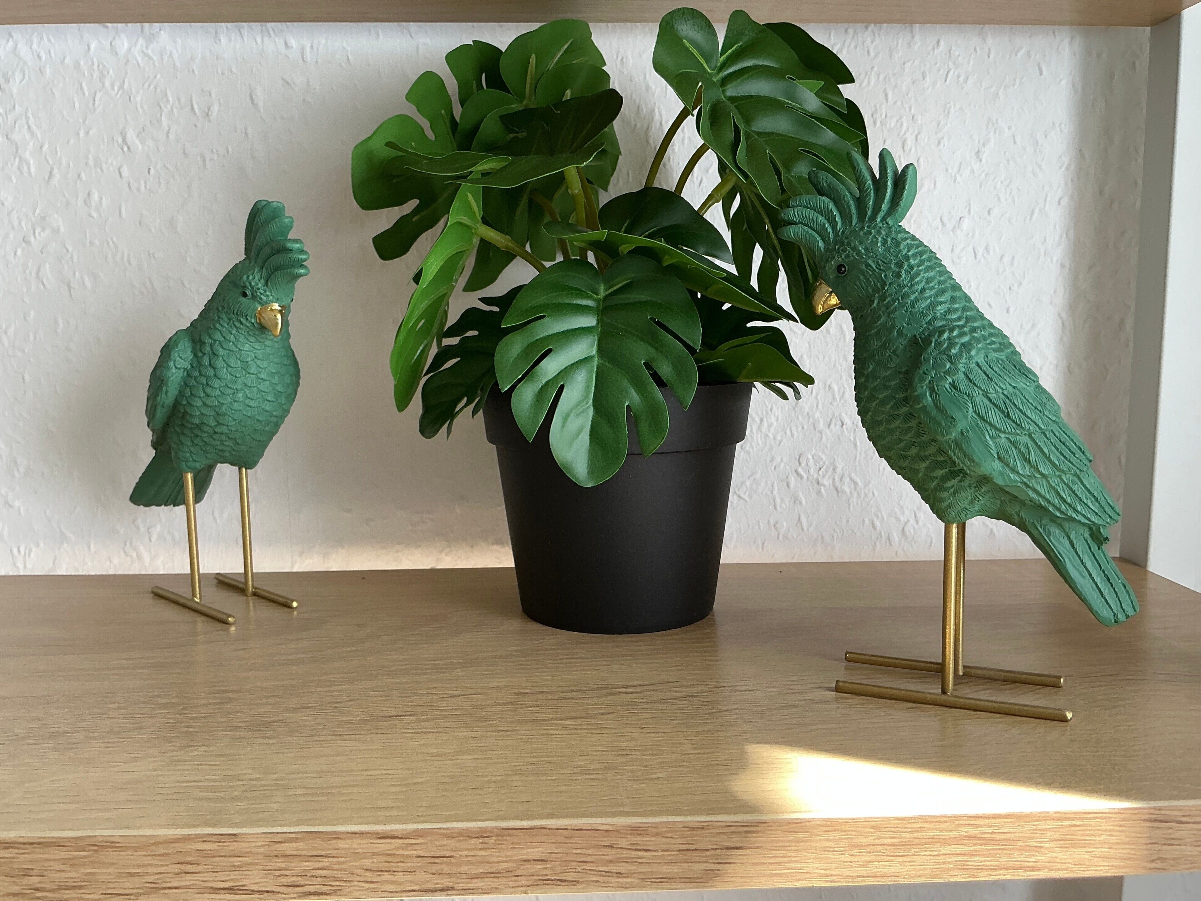 Two green bird sculptures on a wooden shelf with a potted plant.