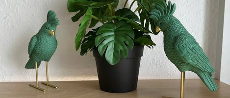 Two green bird sculptures on a wooden shelf with a potted plant.