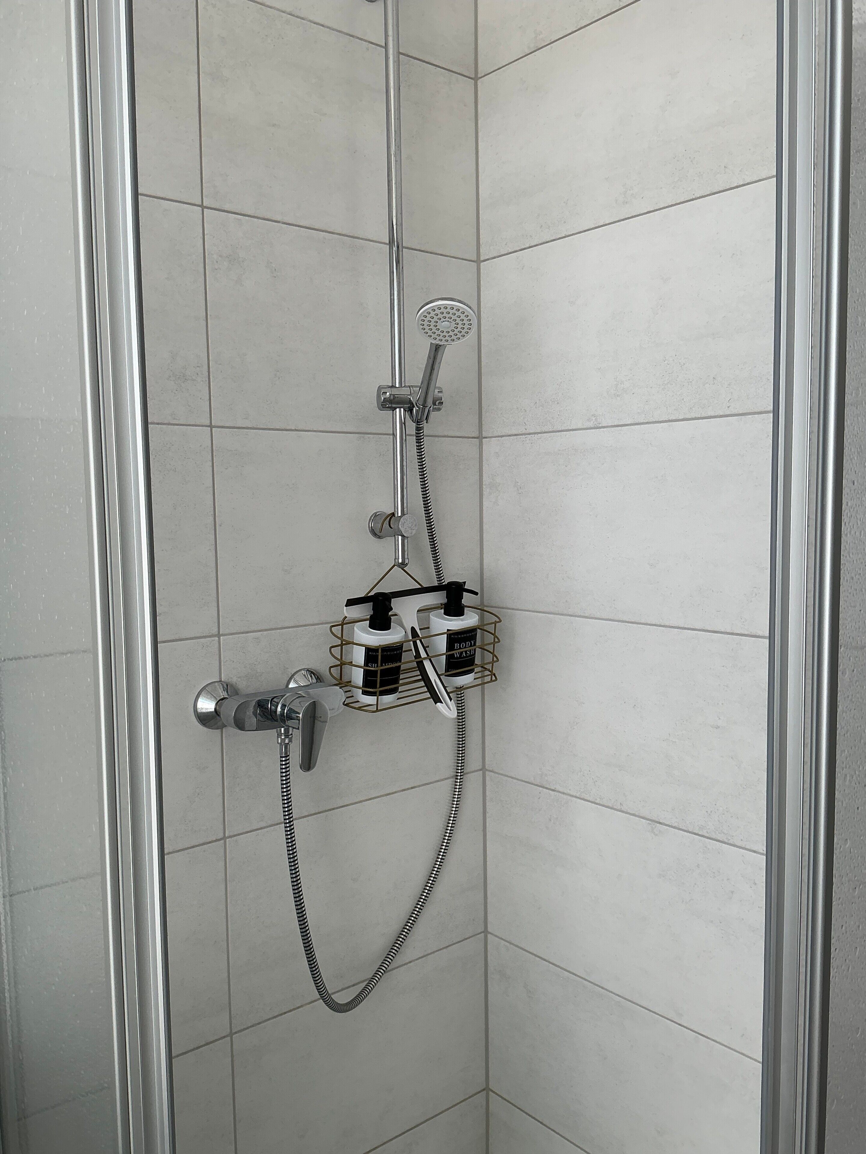 Eine Dusche mit Handbrause, Wandarmatur und einer Duschablage mit Flaschen.
