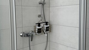 Een douche met een handdouche, een wandmengkraan en een douchemand met flessen.