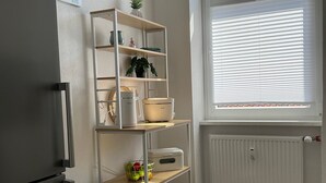 Une cuisine équipée d’un réfrigérateur encastré, d’une fenêtre avec des stores, d’un radiateur blanc et d’une étagère contenant divers objets.