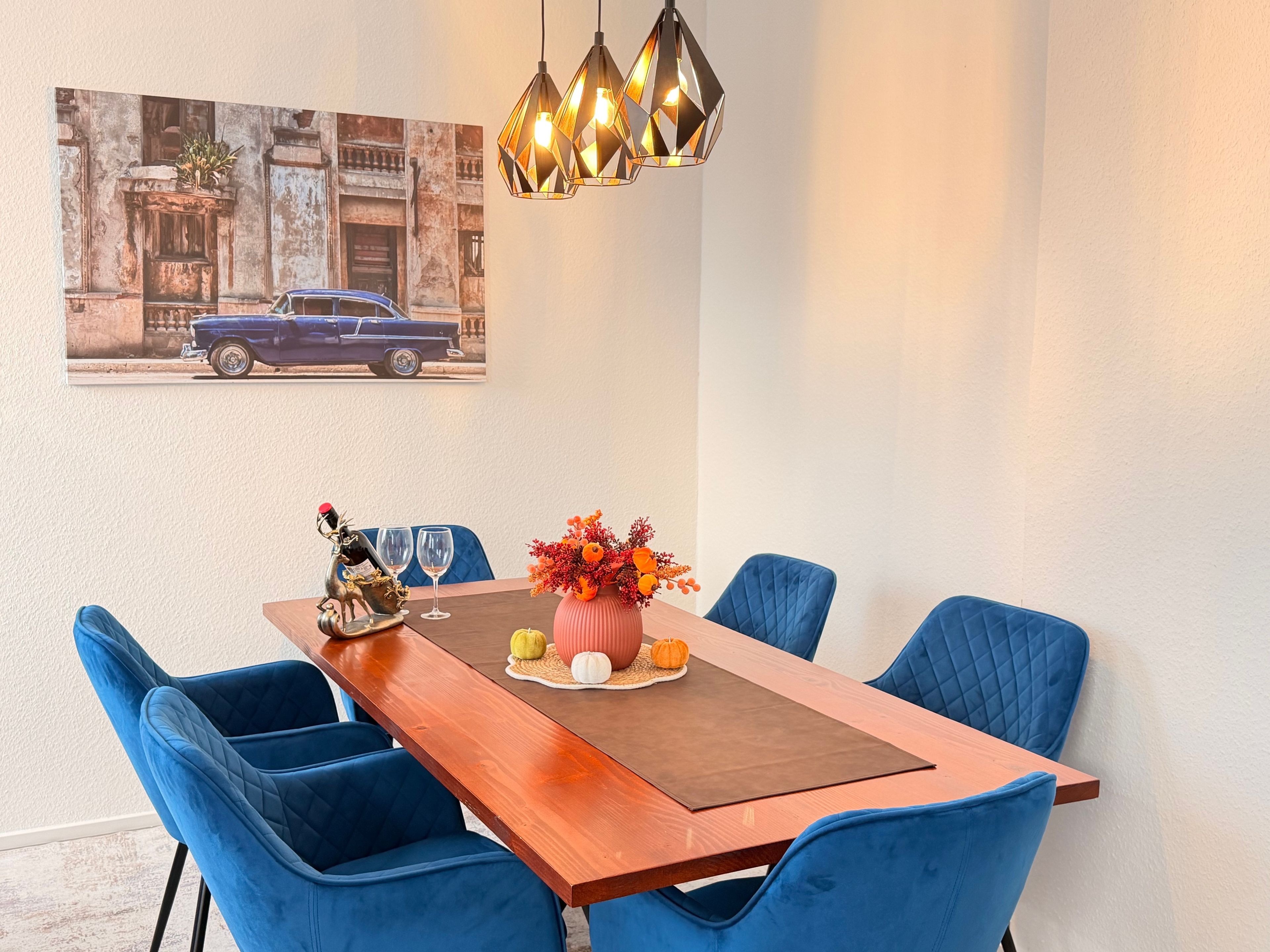 Ein Essbereich mit einem Holztisch, blau gepolsterten Stühlen, einer dekorativen Tischmitte und einer Wandleuchte.