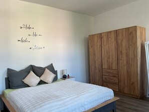Une chambre à coucher avec un lit, des oreillers, une table de chevet, une lampe et une armoire.