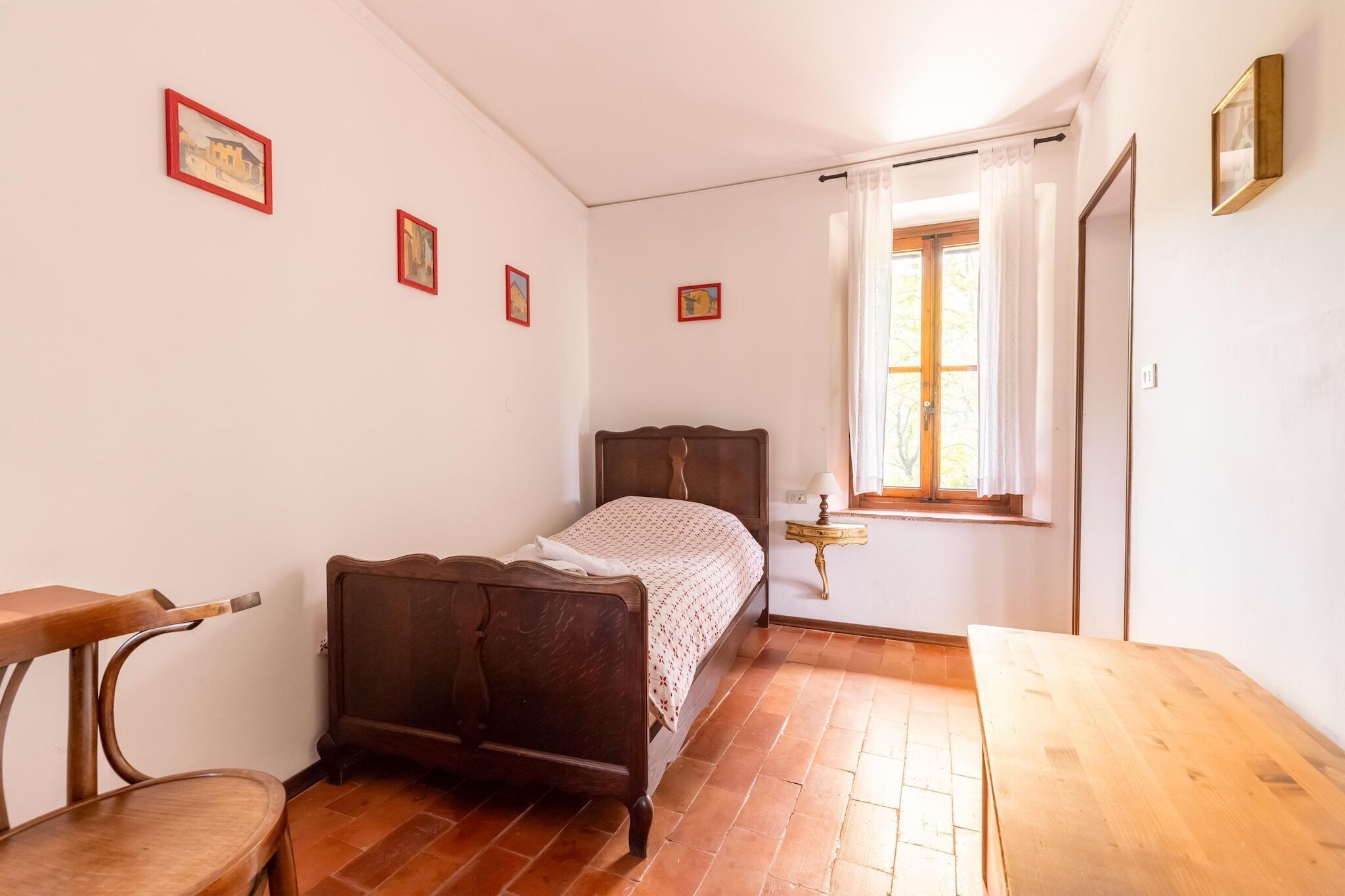 Een slaapkamer met een houten bed, een houten tafel en een raam met gordijnen.