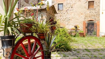 A rustic stone building with a courtyard, potted plants, and a red cart.