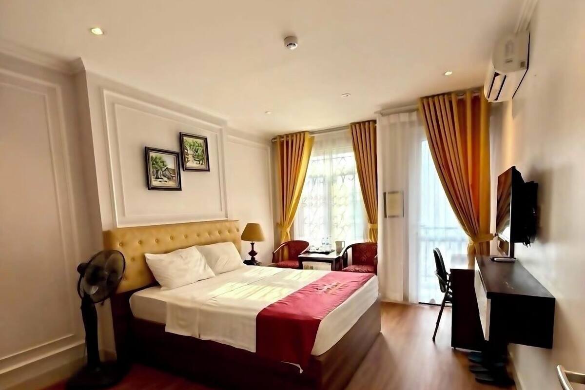 A hotel room with a large bed, a desk, a chair, and a TV.