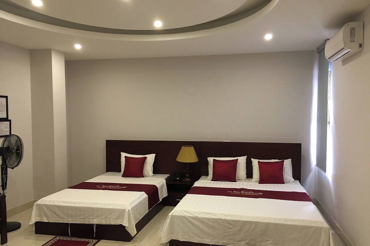 A hotel room with two beds, a ceiling fan, a nightstand, and a window.