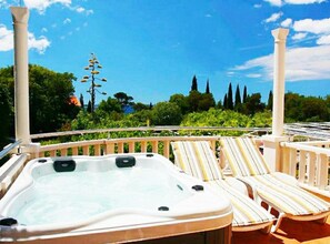 Un bain à remous avec des chaises longues sur un balcon offrant une vue sur les arbres et un ciel dégagé.