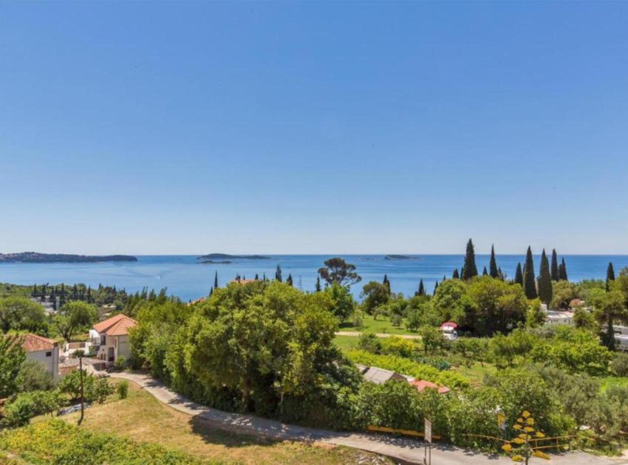 A coastal property with a view of the sea, surrounded by greenery and a few buildings.