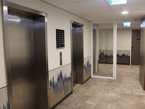 Elevators feature sleek metallic design and a digital control panel, set against a city-inspired wall pattern and light-colored carpet.