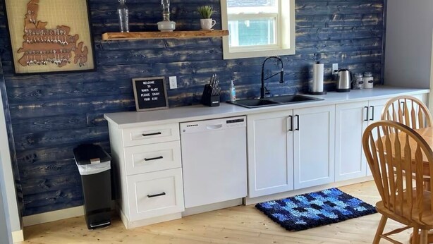 A modern kitchen with wooden cabinets, a built-in window, and a blue rug. - Nan’s Place Vacation Home! Traditional salt box home w/ accessibility ramp (Grand Bank)