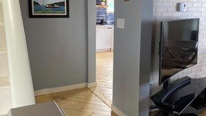 A modern interior with a staircase, a kitchen area, and a TV mounted on a brick wall. - Nan’s Place Vacation Home! Traditional salt box home w/ accessibility ramp (Grand Bank)