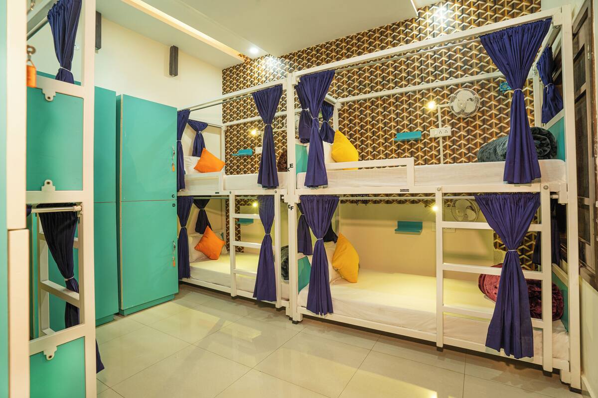 A dormitory room with bunk beds, teal-colored wardrobes, and purple curtains.