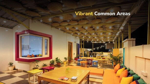 A vibrant common area with a checkered floor, wooden tables, colorful cushions, and hanging baskets. - goSTOPS Amritsar Chatiwind Gate  (Amritsar)