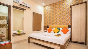 A hotel room with a bed, a wooden headboard, a wardrobe, a mirror, a small table with a plant, and a wall air conditioner. - goSTOPS Amritsar Chatiwind Gate  (Amritsar)