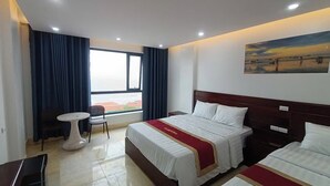 Een hotelkamer met twee bedden, een bureau, een stoel, een bijzettafeltje en een groot raam met gordijnen.