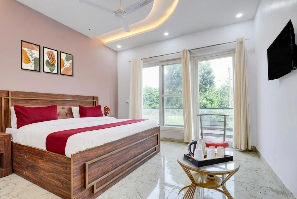 Habitación de hotel con una cama de madera, una mesita redonda con una bandeja, un ventilador de techo y un ventanal con cortinas.