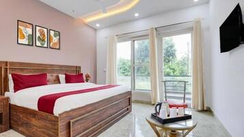 Habitación de hotel con una cama de madera, una mesita redonda con una bandeja, un ventilador de techo y un ventanal con cortinas.