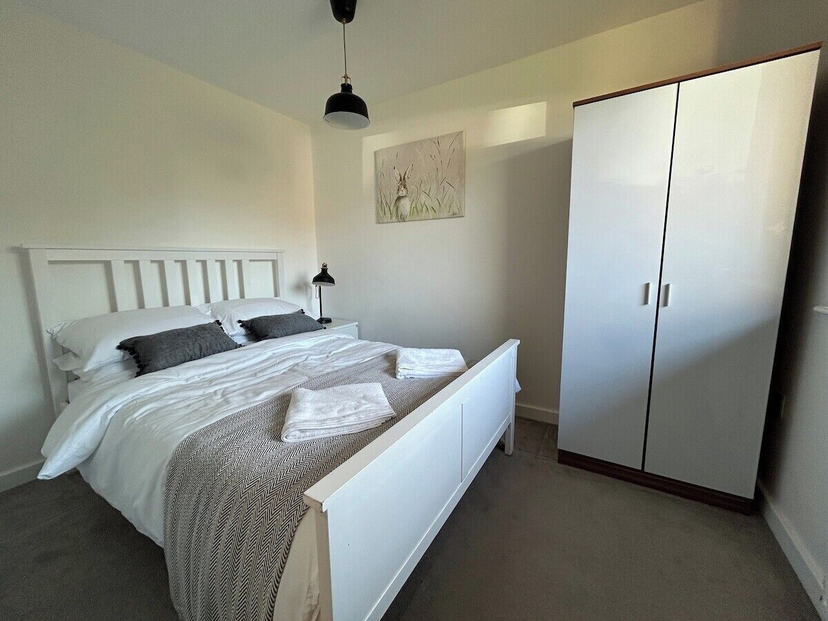 A bedroom with a bed, a wardrobe, a nightstand, a lamp, and a wall-mounted artwork.