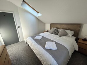 A bedroom with a bed, a nightstand, a bedside table, a wardrobe, and a skylight.