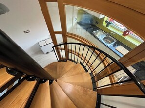 A spiral staircase with wooden steps and black railings, leading to a glass-enclosed balcony with a view of the outside. - Stunning modern home in Lincoln (Lincolnshire)