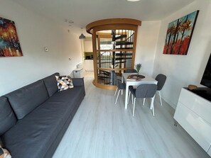 A modern living room with a dark sofa, a dining table with chairs, a white cabinet, and a staircase leading to an upper level. - Stunning modern home in Lincoln (Lincolnshire)
