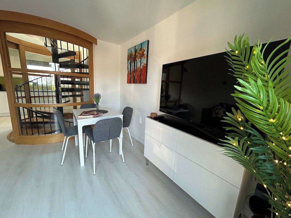 A modern interior with a dining area, a staircase, a flat-screen TV, and a potted plant.