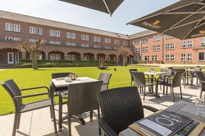 Guests can enjoy the hotel's outdoor seating area with tables and chairs, shaded by trees and umbrellas.