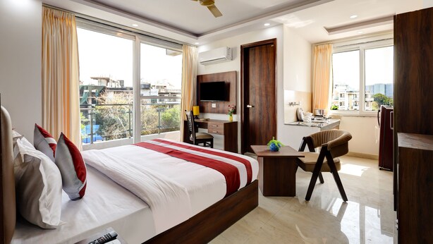 A hotel room with a large bed, a desk, a chair, a TV, and a balcony with a view of the city. - Hotel The Venice- Near Indraprastha Apollo Hospital (New Delhi)