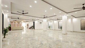 A spacious, well-lit lobby with marble flooring, ceiling fans, and a seating area with a sofa and curtains. - Hotel The Venice- Near Indraprastha Apollo Hospital (New Delhi)