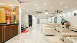 A modern hotel lobby with a reception desk, seating area, and ceiling fans. - Hotel The Venice- Near Indraprastha Apollo Hospital (New Delhi)