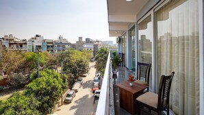 A balcony with a table and chairs, overlooking a street with parked cars and buildings. - Hotel The Venice- Near Indraprastha Apollo Hospital (New Delhi)