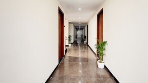 A long, narrow hallway with a polished floor, wooden doors, and potted plants. - Hotel The Venice- Near Indraprastha Apollo Hospital (New Delhi)