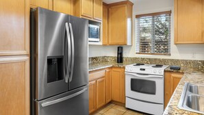 A kitchen with wooden cabinets, stainless steel appliances, a granite countertop, and a window with blinds.