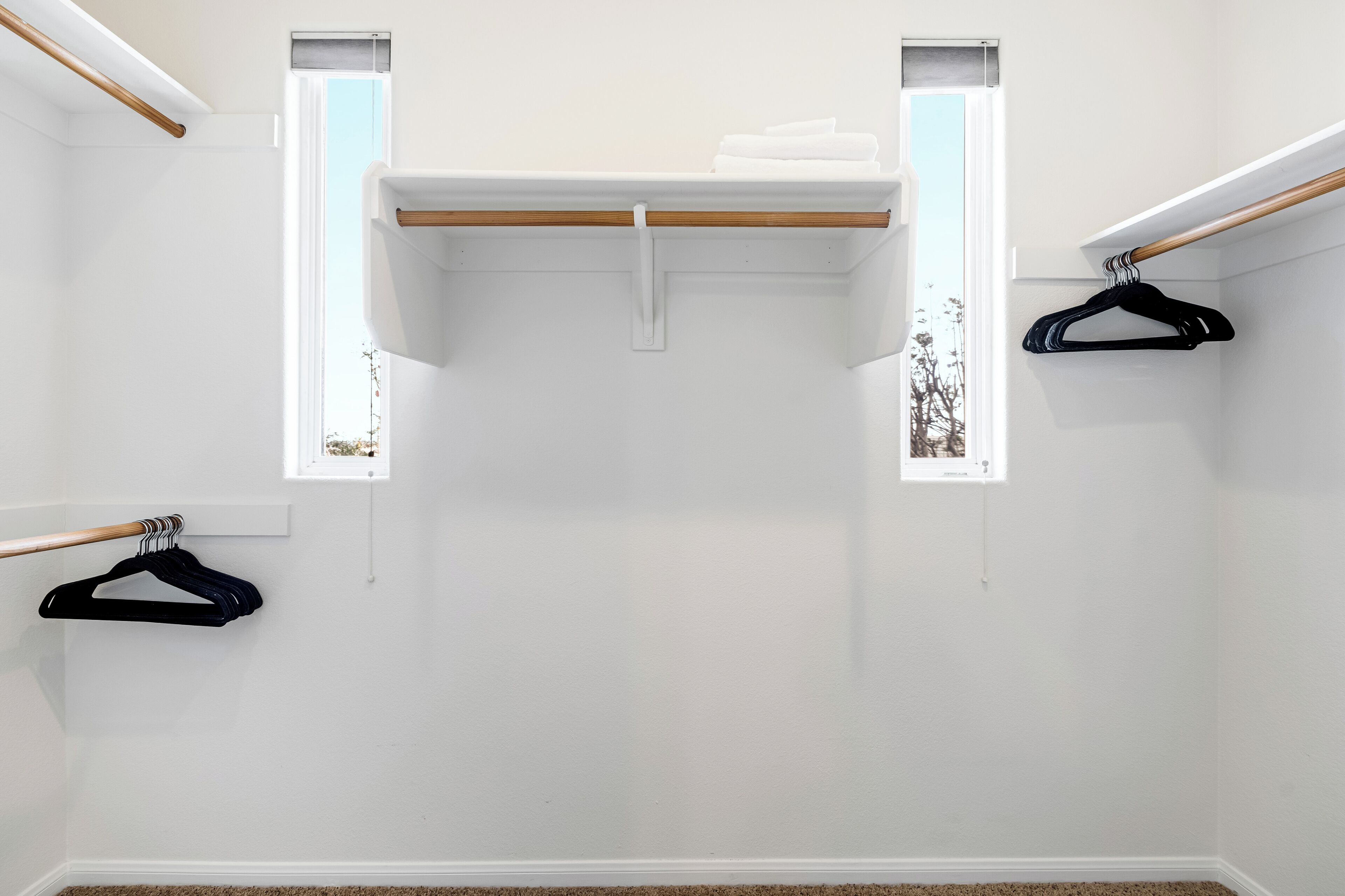 Une pièce avec un mur blanc, une poutre en bois, une étagère blanche et deux fenêtres.